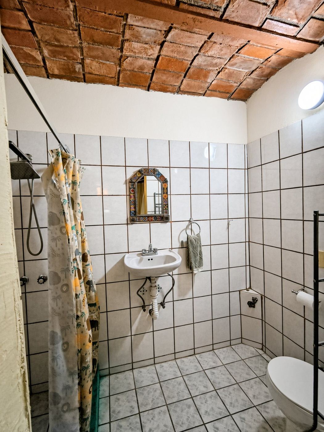 A bath at La Casa Grande, white tile, a brick ceiling, and a painted shower curtain
