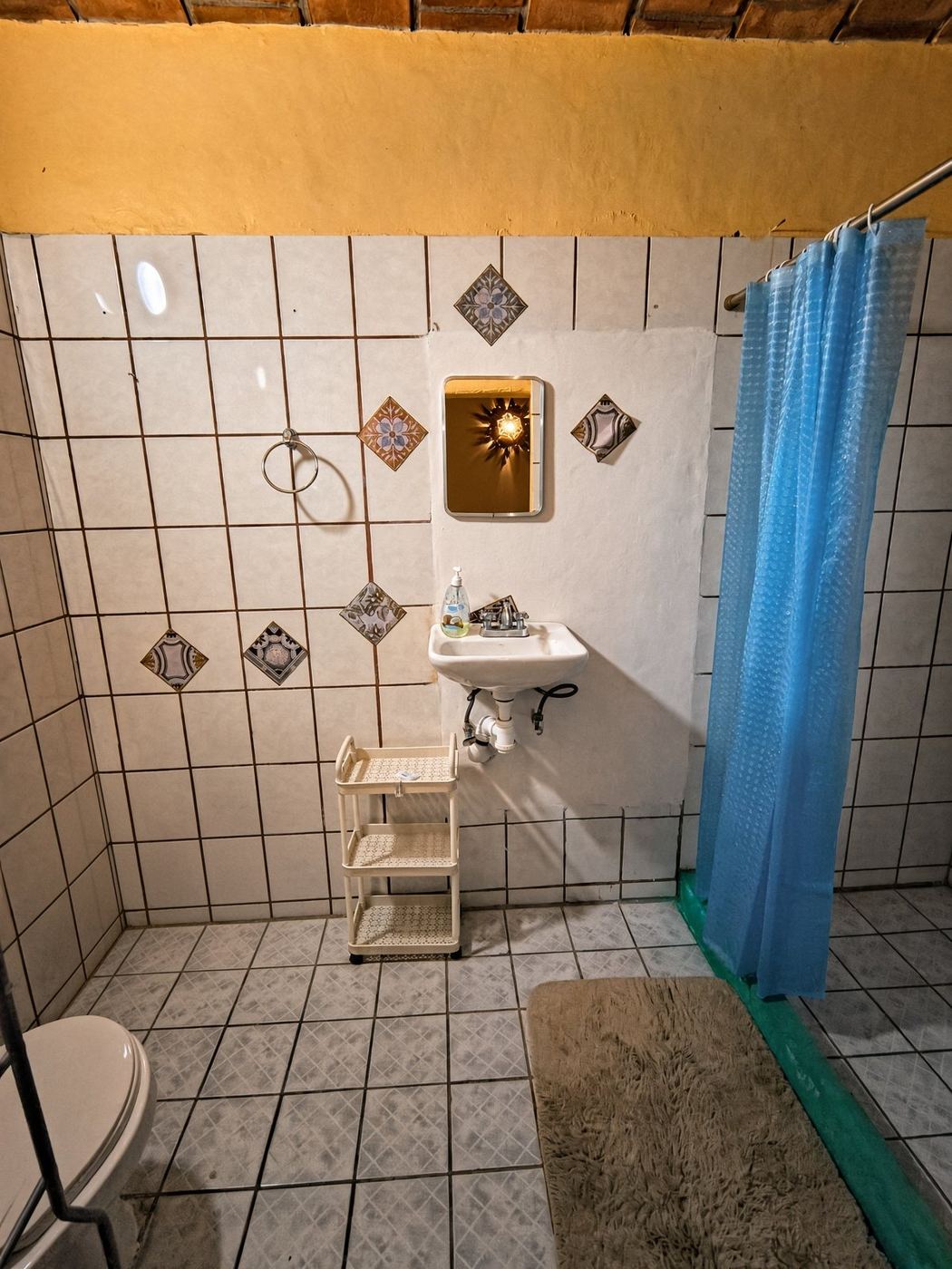 A bath at La Casa Grande, mustard wall, patterned accent tiles, and a blue curtain