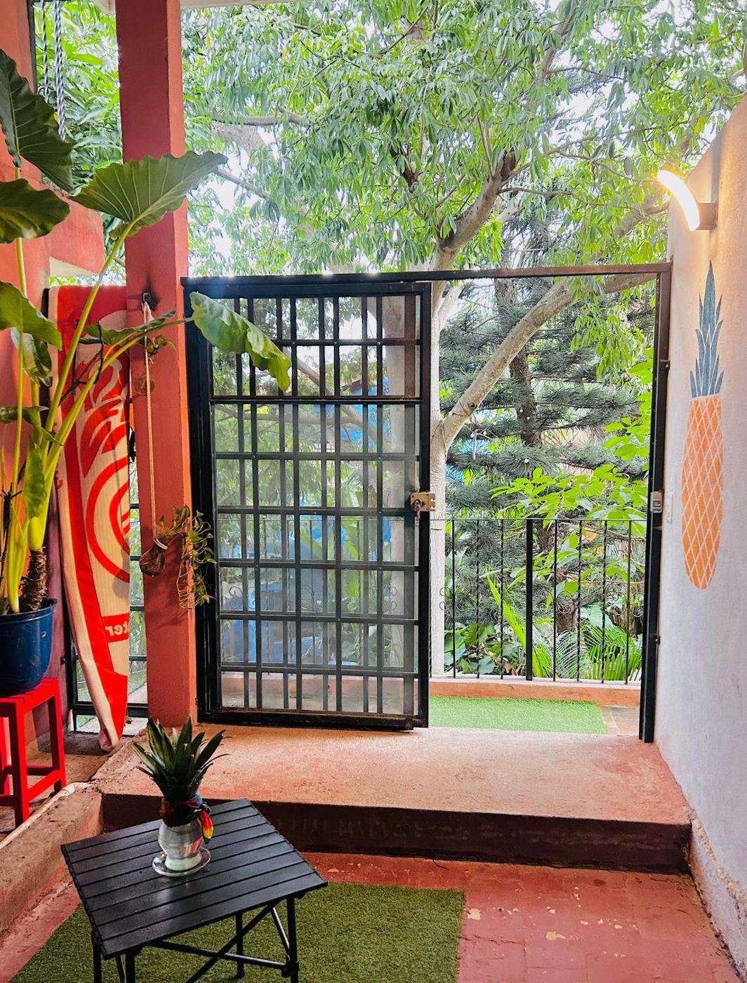 The black gate at El Loft, open to the trees, with a pineapple painted on the white wall